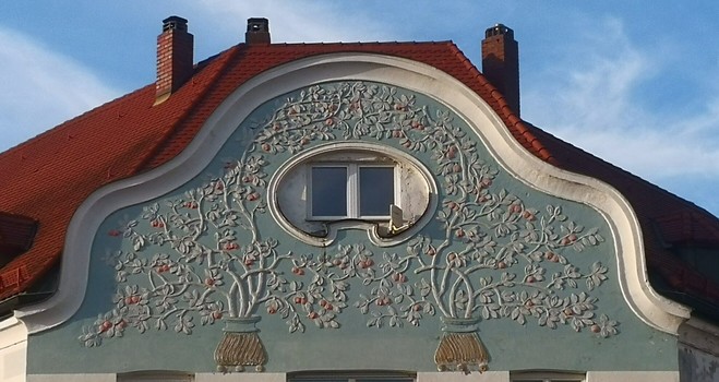 Hausdachfassade mit ovalem Fenster, umrinkt von Blumendekor.