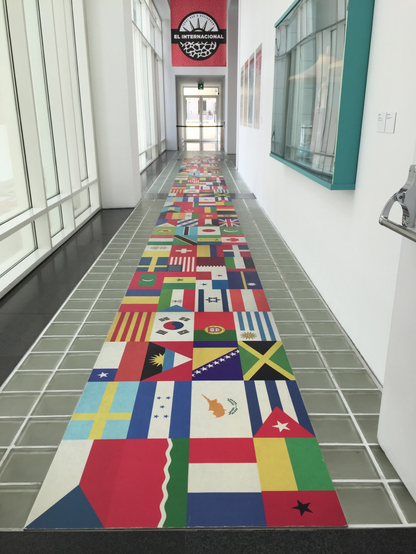 Long hallway with flags from many nations arranged like a carpet on the floor leading to a window in a museum in Barcelona, Spain.
