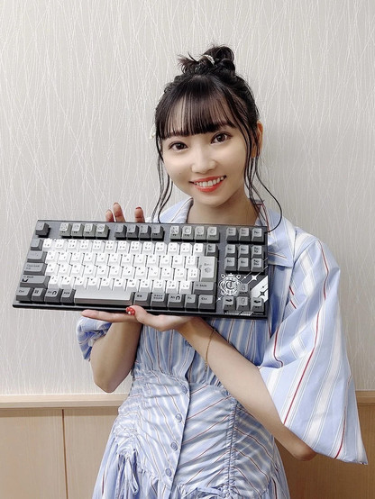 Hinaki smiling as she shows off a Uma Musume themed mechanical keyboard.