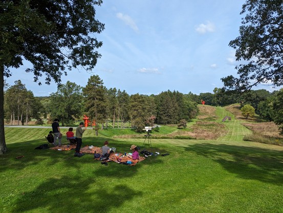 A view of storm king sculpture garden with a group of people sitting in the foreground on picnic blankets making art