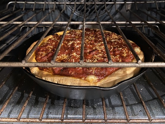 A deep dish pizza in a cast iron pan in the oven
