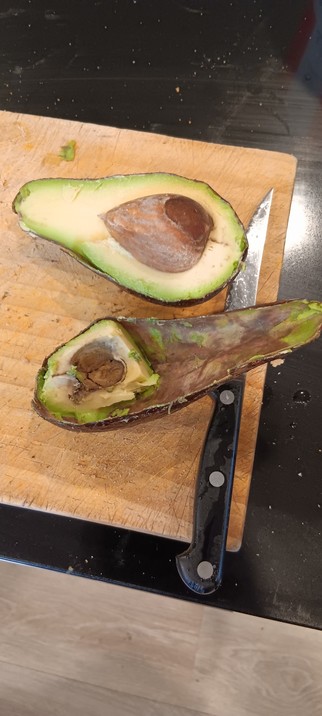 A cut open avocado on the chopping board next to a knife