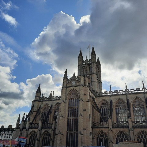 Bath Abbey, with the golden stone and magnificent arched windows standing out against a blue sky with grey and white cumulus and cumulonimbus clouds