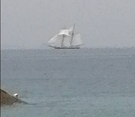 on a grey sea under a grey sky, a sailboat far away on the horizon, masts and sails deployed, a classic shape from past centuries