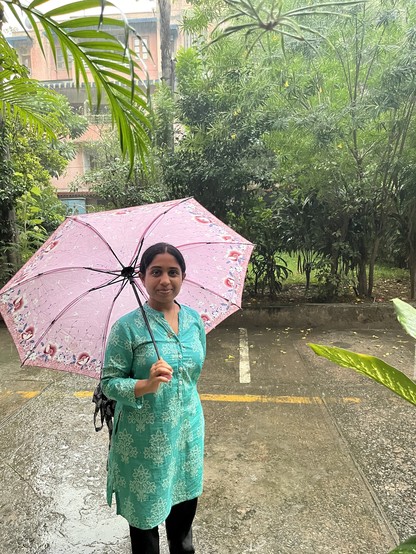 Ruchika standing in the rain under a pink umbrella in a teal kurti.
