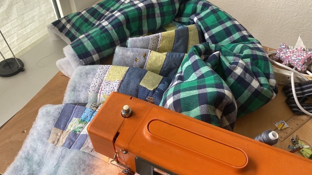 A roll of fabric and batting is under an orange sewing machine. The machine and fabric are sitting on a very messy table.