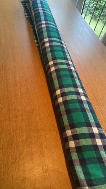 A piece of fabric in a long roll lying on a table. The fabric is plaid flannel in green, blue and white.