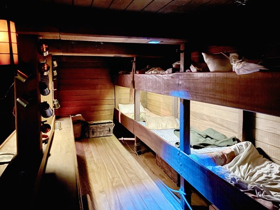 Recreation of below-decks accomodation on a migrant ship, with end-to-end bunk beds & a central bench for taking meals etc.