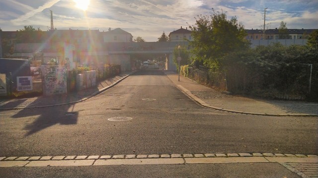 Eine leere Straße gegen die Sonne fotografiert. Im der Mitte eine Bahnunterführung.