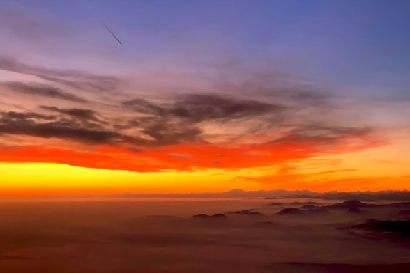 Glorious sunset while crossing the Alps. the valleys below are covered in fog, only the mountain ranges are visible. Yellow and red fade into dark clouds and violet sky above.