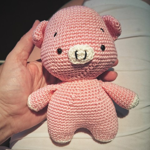 Small crocheted pink pig toy laying on an outstretched hand.