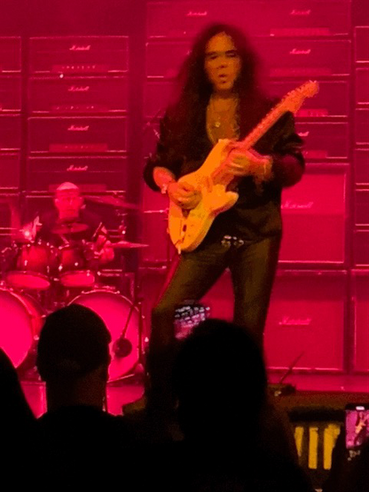Guitarist Yngwie Malmsteen playing a guitar solo on stage.