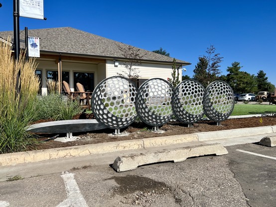 One of three “Ace!” sculptures, installed. Each sculpture consists of four stop-motion views of a golf ball rolling into the cup. The dimples of the ball’s surface are represented by rounded hexagonal cuts, with a crescent of dark metal for the shadow.
