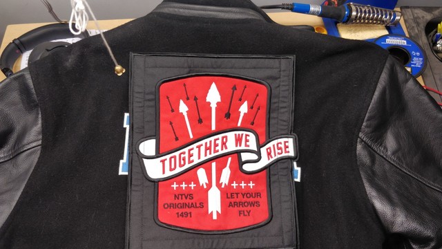 Black jacket with patch on back, that reads "together we rise".