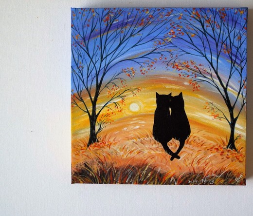 Two black cats sitting on an autumnal colored meadow with tails entwined