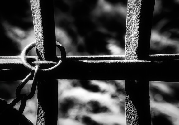 Ein altes rostiges Gitter an deren rechter Seite eine Kette befestigt ist. Das Foto ist in Schwarzweiß.