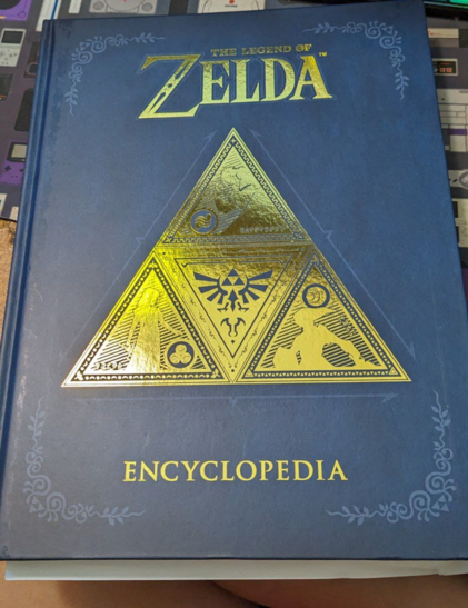 The cover of the Zelda encyclopedia. There's a triforce on the front. The book is a large hardcover book.