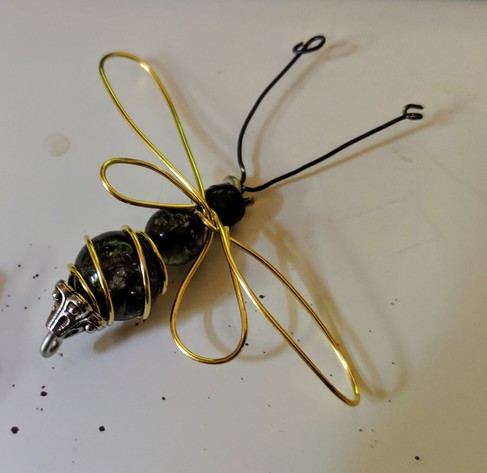A wire wrapped bee with beads for the head, thorax, and abdomen, black wire for antennae, and gold wire for wings and stripes.