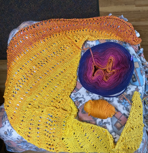 Lacy knitted scarf going from yellow to orange to pink with ball of orange cut out from cake of yarn that has pink purples and blue to use