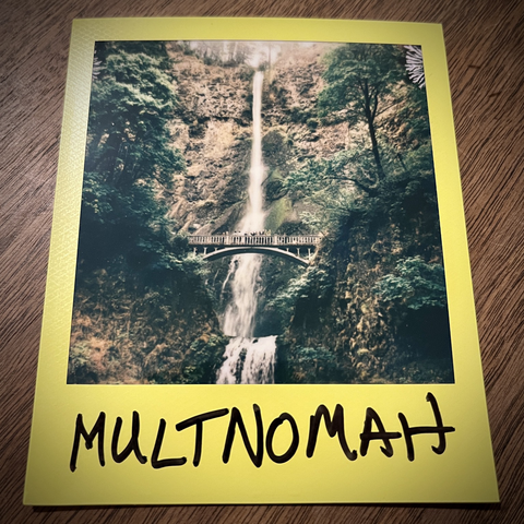 A Polaroid photo captures Multnomah Falls, with visitors waving from Benson Bridge.