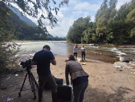 A film team recording researchers how they sample microplastics in a river.