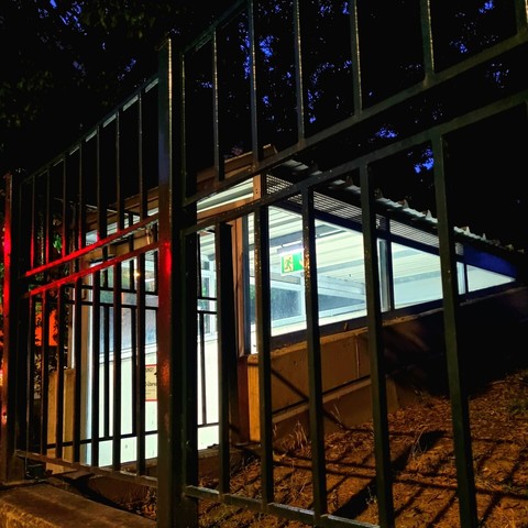 Illuminated entrance to a parking garage behind a solid fence in the evening. The picture's left part has a red glow resulting from the adjacent traffic light.