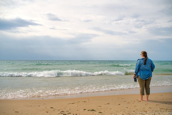 A woman stands on the beach facing the waters of Lake Michigan.