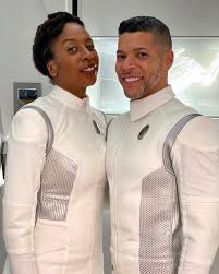 A torso and head shot of Raven Dauda (LHS) as Dr Tracy Pollard and Wilson Cruz (RHS) as Dr Hugh Culber in their white Discovery medical officers’ uniforms of seasons 2 & 3.