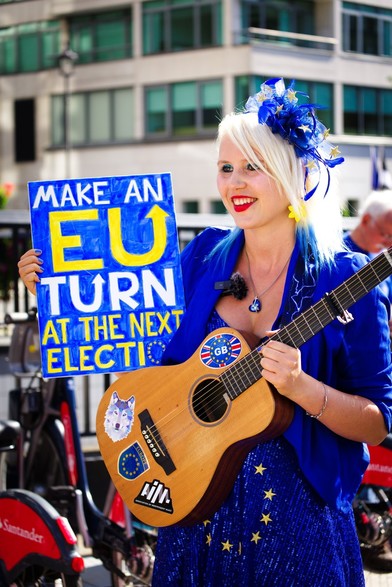 Madeleina Kay at the march to rejoin, dresses all in blue and yellow featuring the EU flag stars, holding a guitar plastered with pro-EU stickers, and a sign reading, "Make an EU turn at the next election."