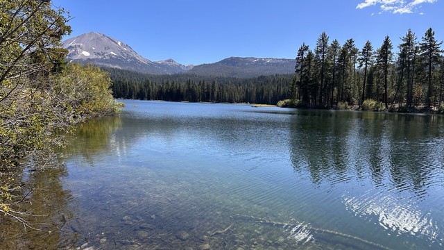 Clear water in Manzanita lake reflecting clouds and blue sky with Lassen peak looming in the background