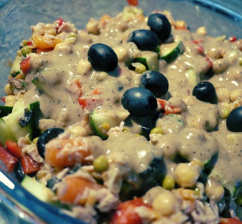 Photo of a chickpea, tuna and vegetables salad with a brown sauce and black olives on top.