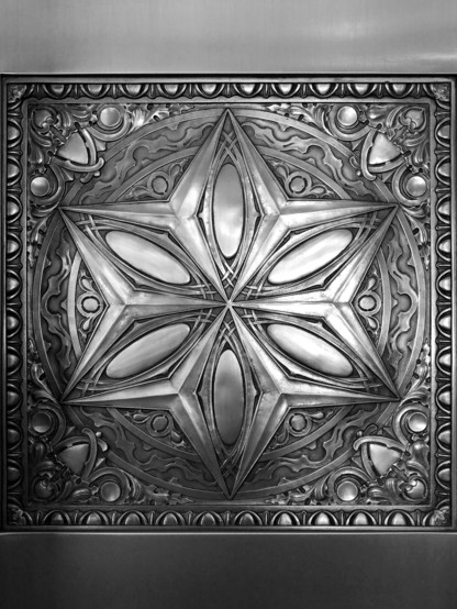 Black and white photo of square metal panel featuring a decorative motif consisting of a six pointed star superimposed over a circle