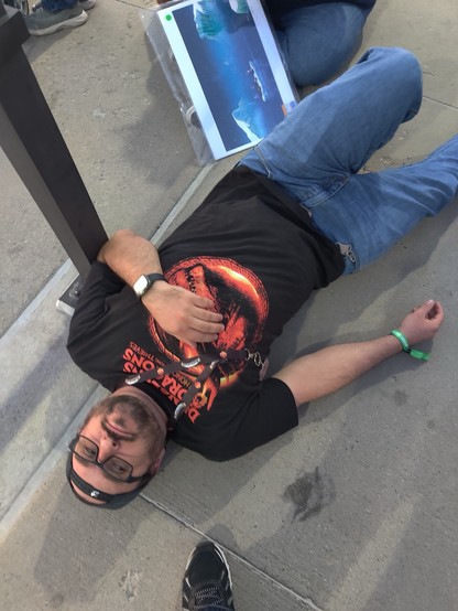 A man wearing a Dungeons And Dragons Honor Among Thieves shirt laying on concrete.