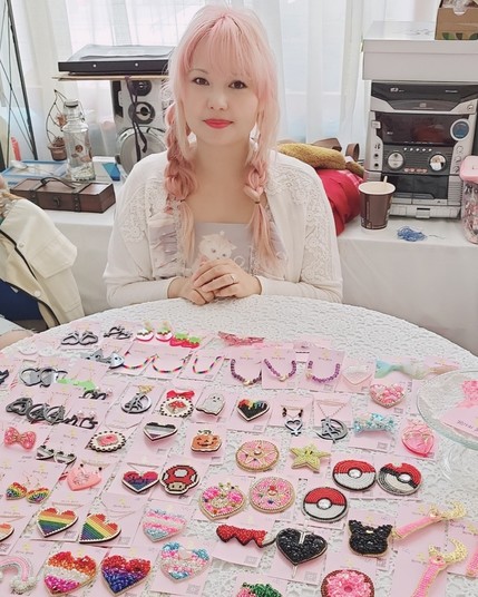 woman with pink hair sitting at a round tavle with small jewelry pieces pinned on cards before her.