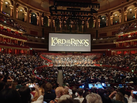 A picture of the inside of the royal Albert hall, with the crowd, orchestra, and a display with the text "The lord of the rings: the two towers"