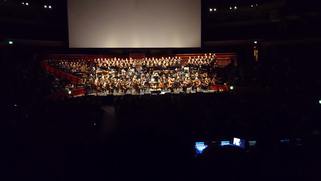 A video of the inside of the royal Albert hall, with the crowd, orchestra, with an orchestra playing along with the beginning of the two towers on screen