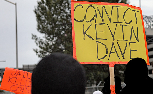 Photo of protesters and signs, Convict Kevin Dave yellow sign, Jail Killer Cops orange sign.