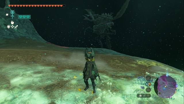 A screenshot from Zelda Tears of the Kingdom. Link is looking toward the camera, while a massive boss monster can be seen in the background of the depths.