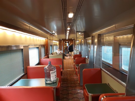 New York Central 43. It is a bar and lounge car built in 1947. This photo is taken in front of the bar looking down the car with tables in the foreground and a seating area in the background.