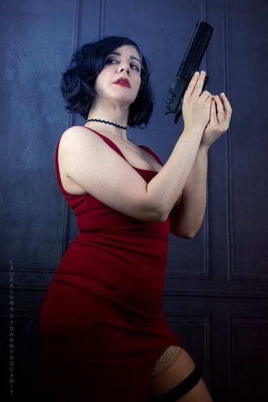 Laura con un vestido rojo y gargantilla, sujeta una pistola, en guardia. El vestido es escotado, con escote cuadrado y tiene una apertura lateral.