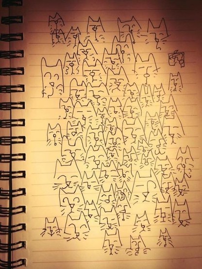 A lined pad of paper packed with cat's faces drawn in black ink, becoming less dense towards the edge of the page. Some cats look happy, others nonplussed, others surprised, a few elegantly detached, and so on.