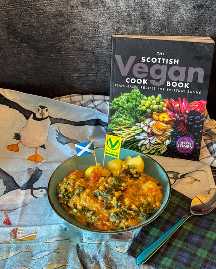 Teller mit Grünkohl und roten Linsen, darin stecken eine Schottische und eine Veganfahne. Tischdecke mit Papageintauchern. Buch: The scottish vegan cook book.