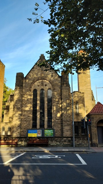 Golden light on an autumn evening, making the old stonework of the Italianate architecture of Morningside United Church glow, while dappled shadows from a tree opposite are cast on the facade