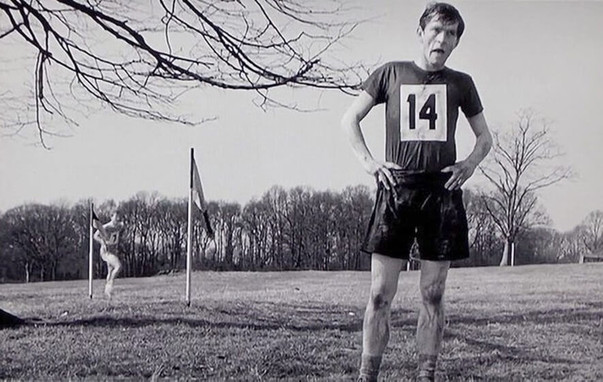 long-distance facilitator. Black and white movie image of Colin Smith, the protagonist of the 1962 film "The Loneliness of the Long Distance Runner". Smith is wearing running clothes with the number 14 on his chest, standing in a field with flags and another runner behind him.
