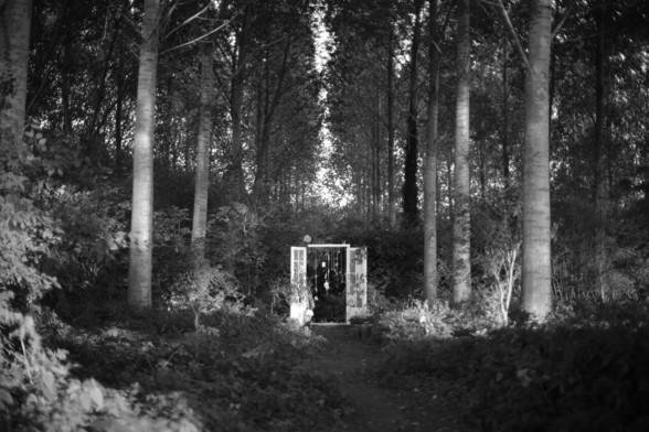 An installation of a portal in a forest, with ritual objects hanging in it.