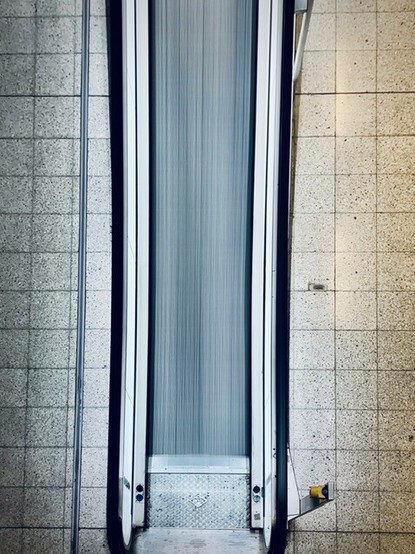 Rolltreppe am Düsseldorfer Flughafen von oben gesehen. Die Konturen des Rollbandes verschwimmen optisch durch eine Langzeitbelichtung.
