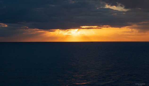 A golden sunset shines through dark clouds above a dark sea.