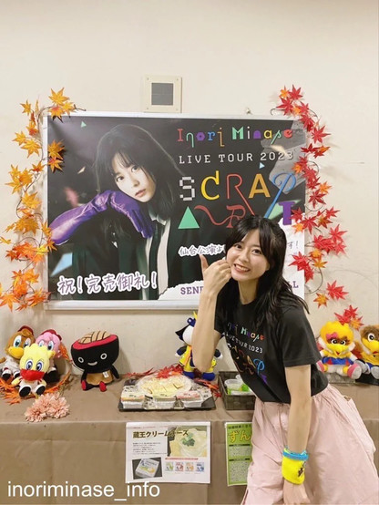 Inori smiling posing in a poster for her tour with stuff on the table.