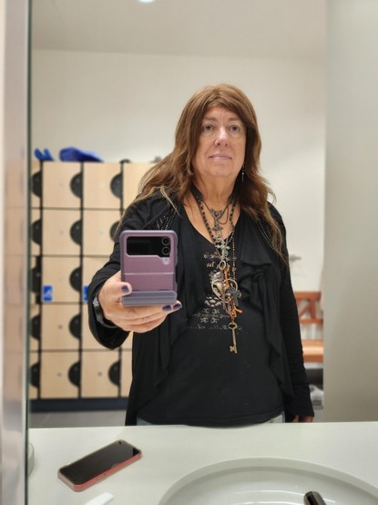 Selfie holding my purple phone. I'm wearing all black,  like me heart,  and too many necklaces as usual

Small lockers are in the background