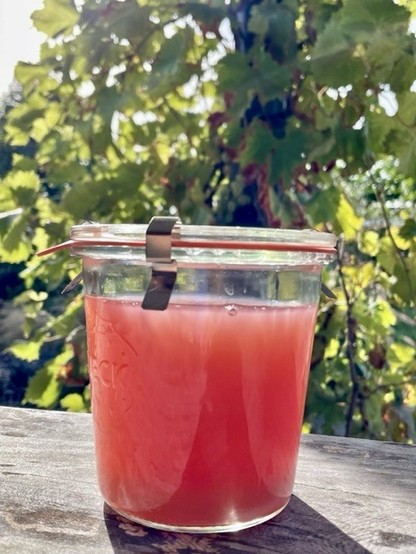 grape juice in a weck jar on the wooden garden table, with the vine in the background